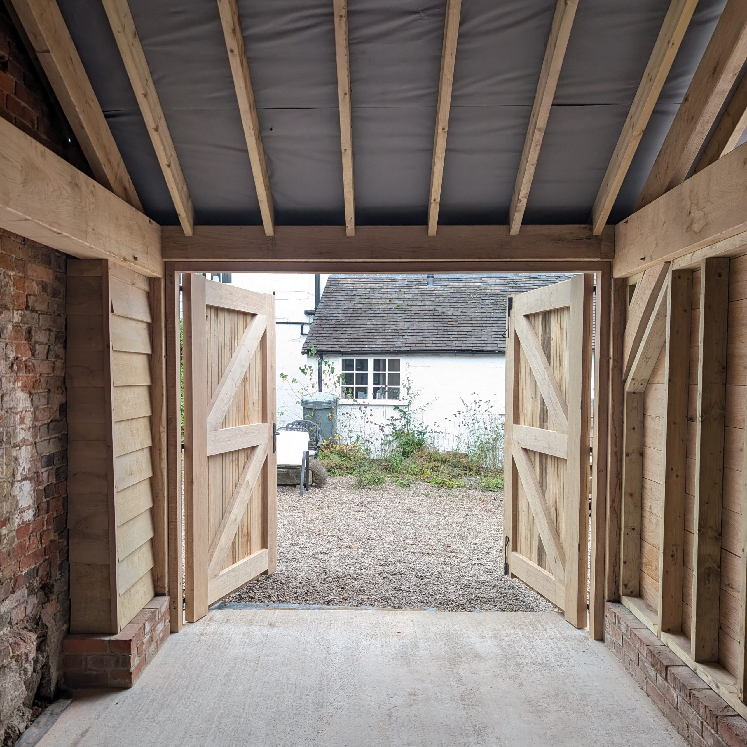 Interior view of a 1-bay timber garage under construction showing the structural frame, rafters, and open wooden double doors.