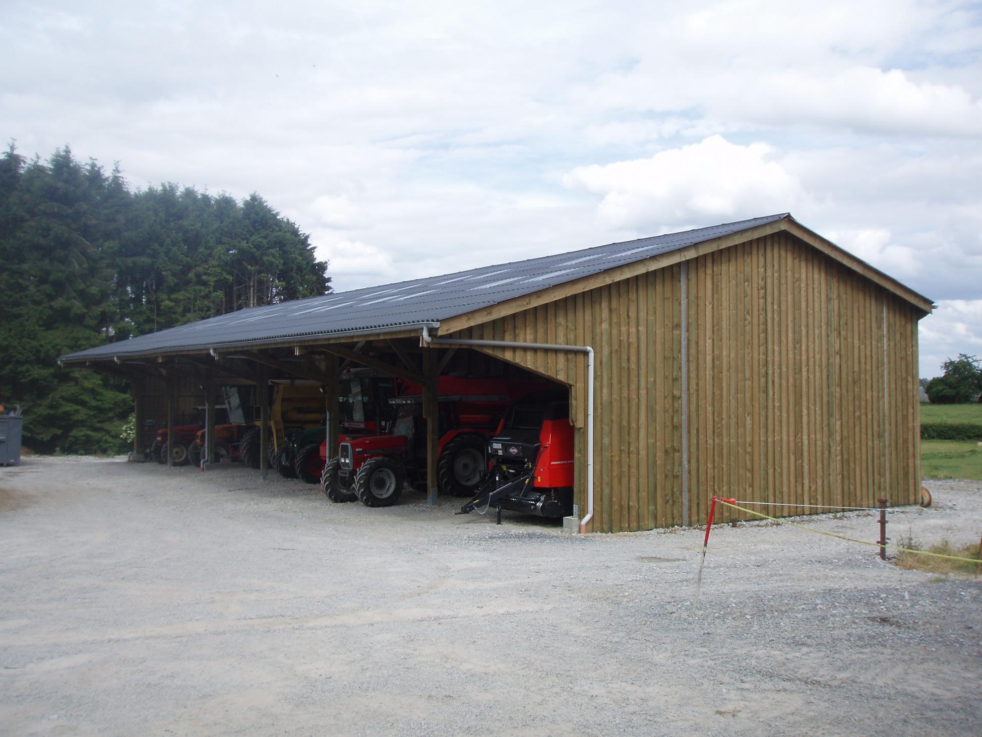 Large timber frame agricultural building with vertical cladding housing several tractors and farm machinery under a mono-pitch roof.