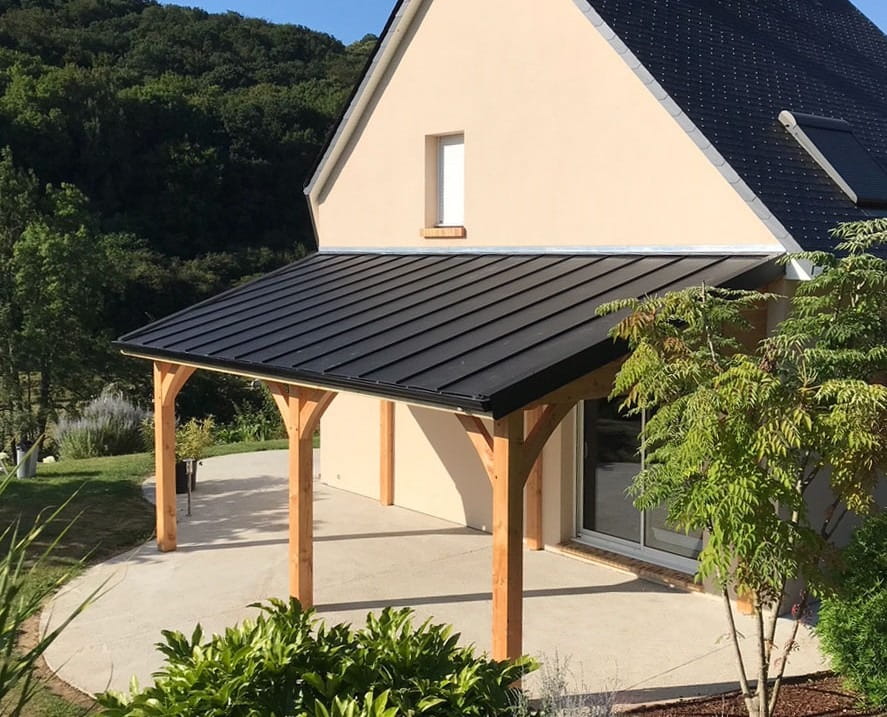 A modern timber-framed lean-to veranda with a black metal roof attached to the side of a contemporary cream-colored house.
