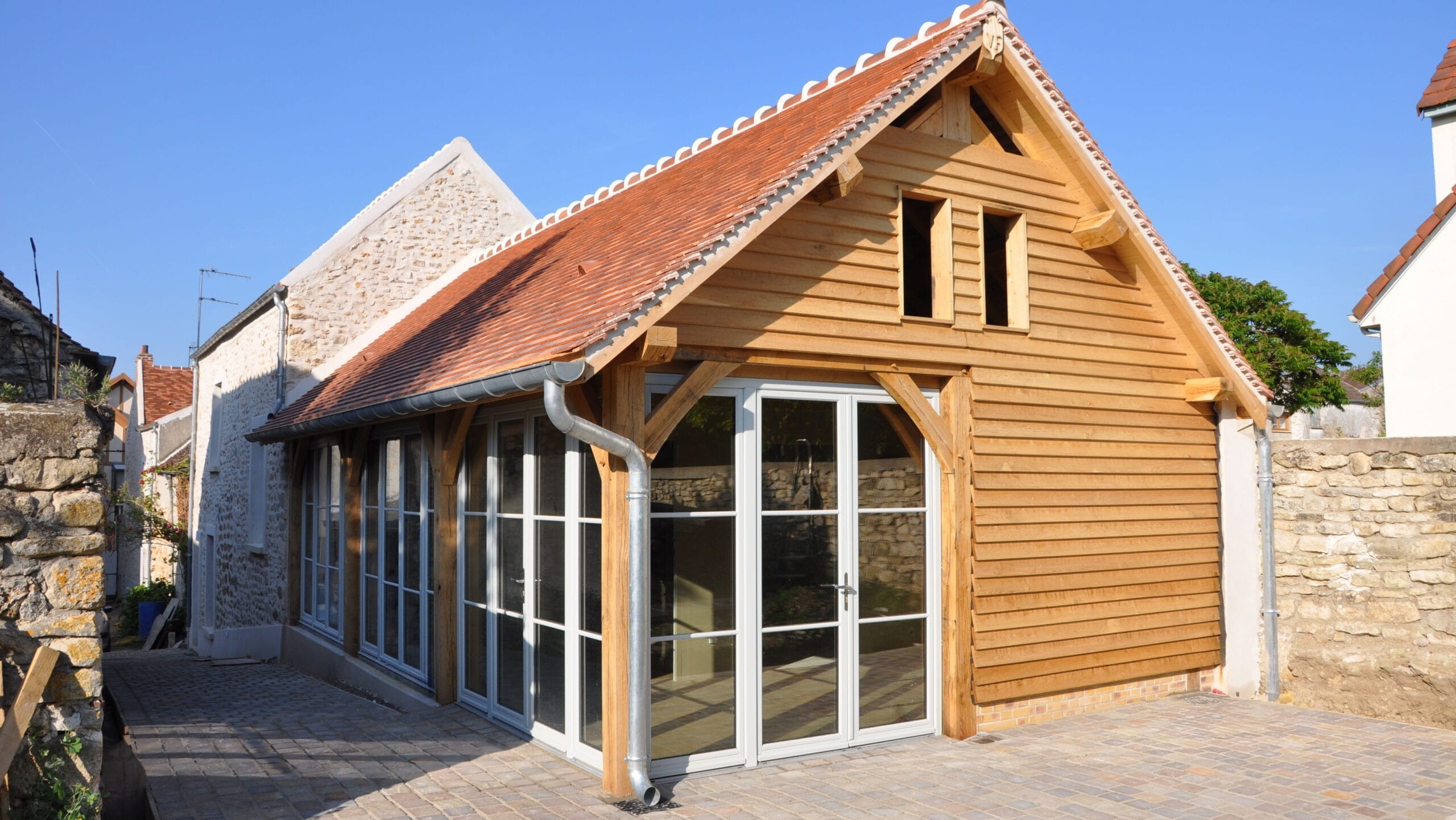 A large, fully enclosed and insulated oak-framed garden room with timber cladding, white French doors, and a red tiled roof.