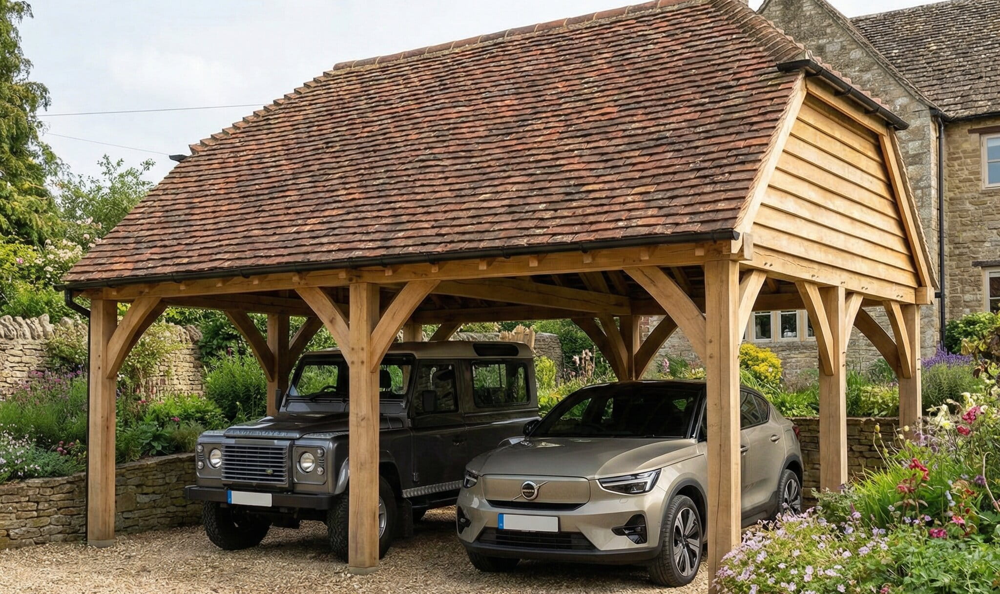An open-sided oak timber carport housing a vintage 4x4 and a modern SUV, featuring a traditional tiled roof and curved bracing.