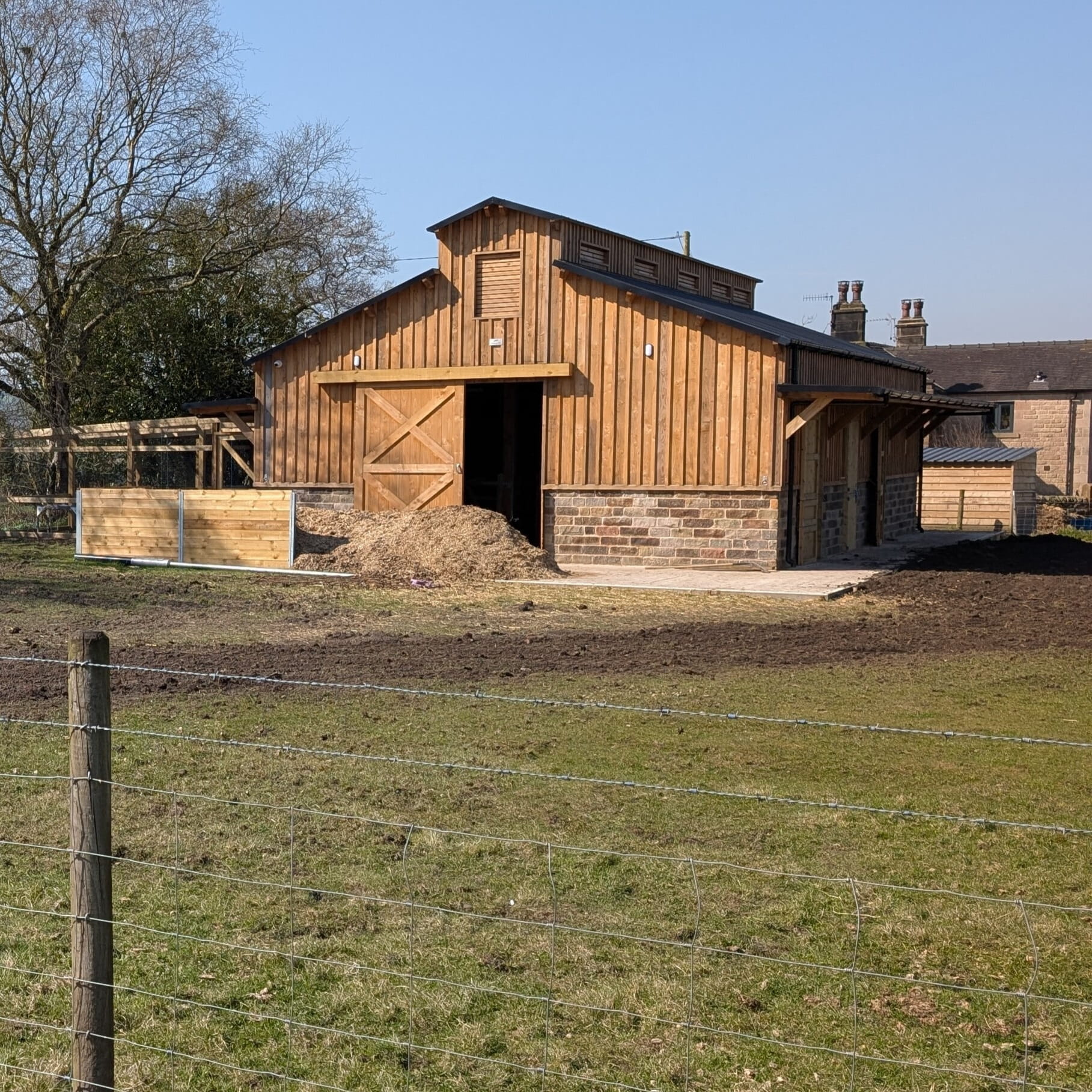 A classic two-story traditional timber barn with stone foundations and large wooden doors, set in a rural landscape.