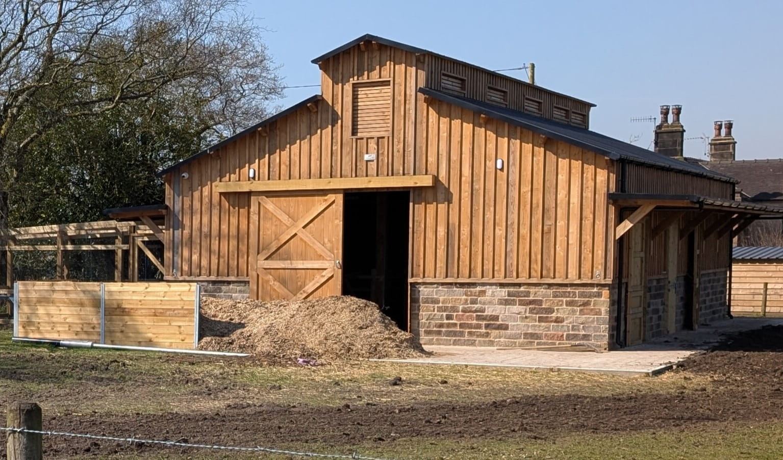 A large traditional timber barn with a pitched roof, vertical wood cladding, and a stone base, featuring large sliding barn doors.