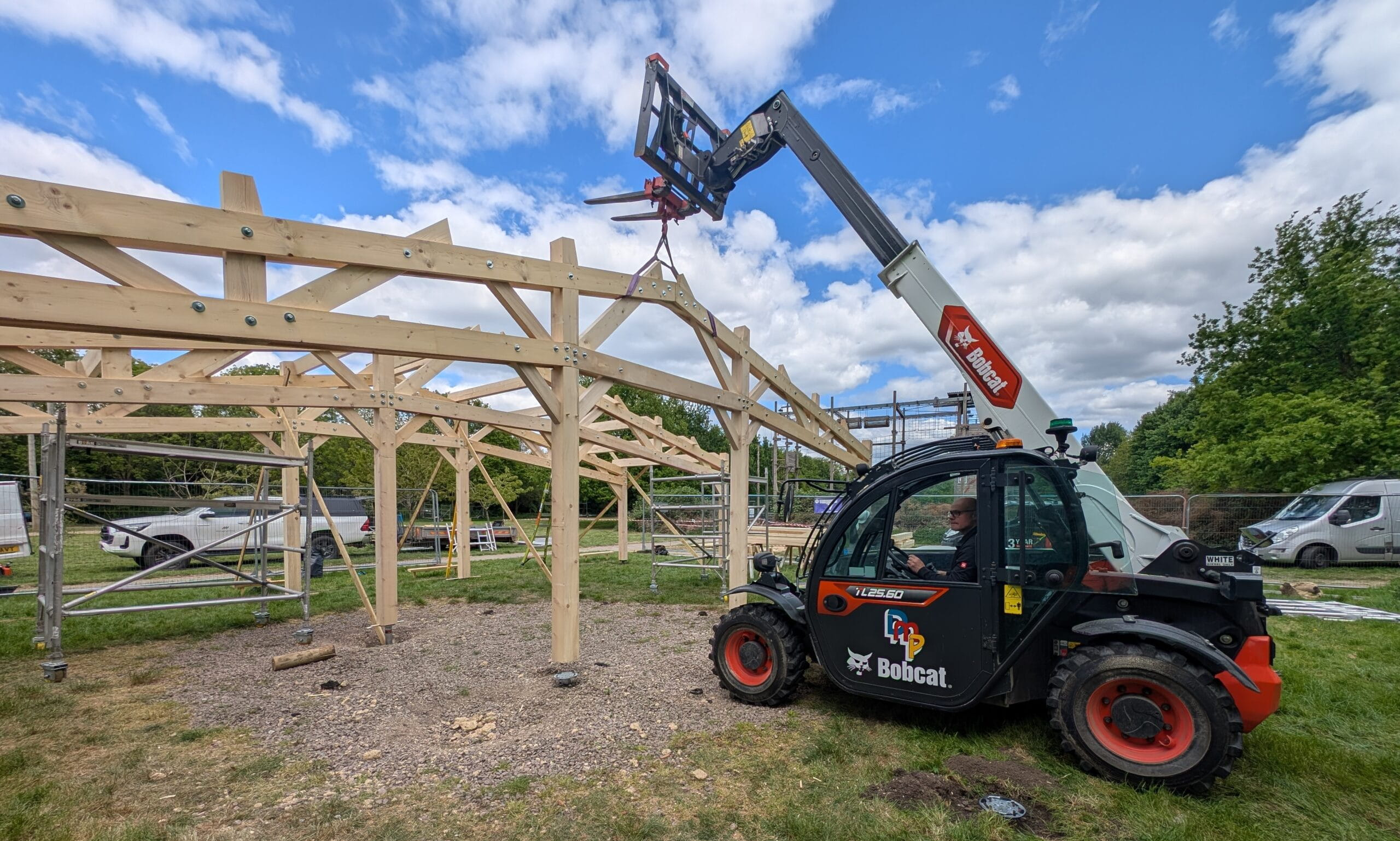 A Bobcat telehandler lifting a timber truss into place during the rapid on-site assembly of a large oak-framed structure.