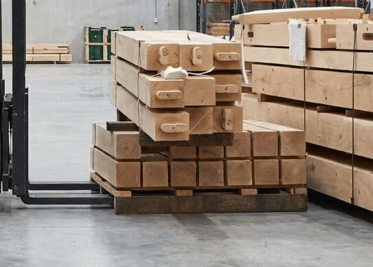 A stack of precision-machined oak posts and beams organized on a wooden pallet in a warehouse, ready for shipping.
