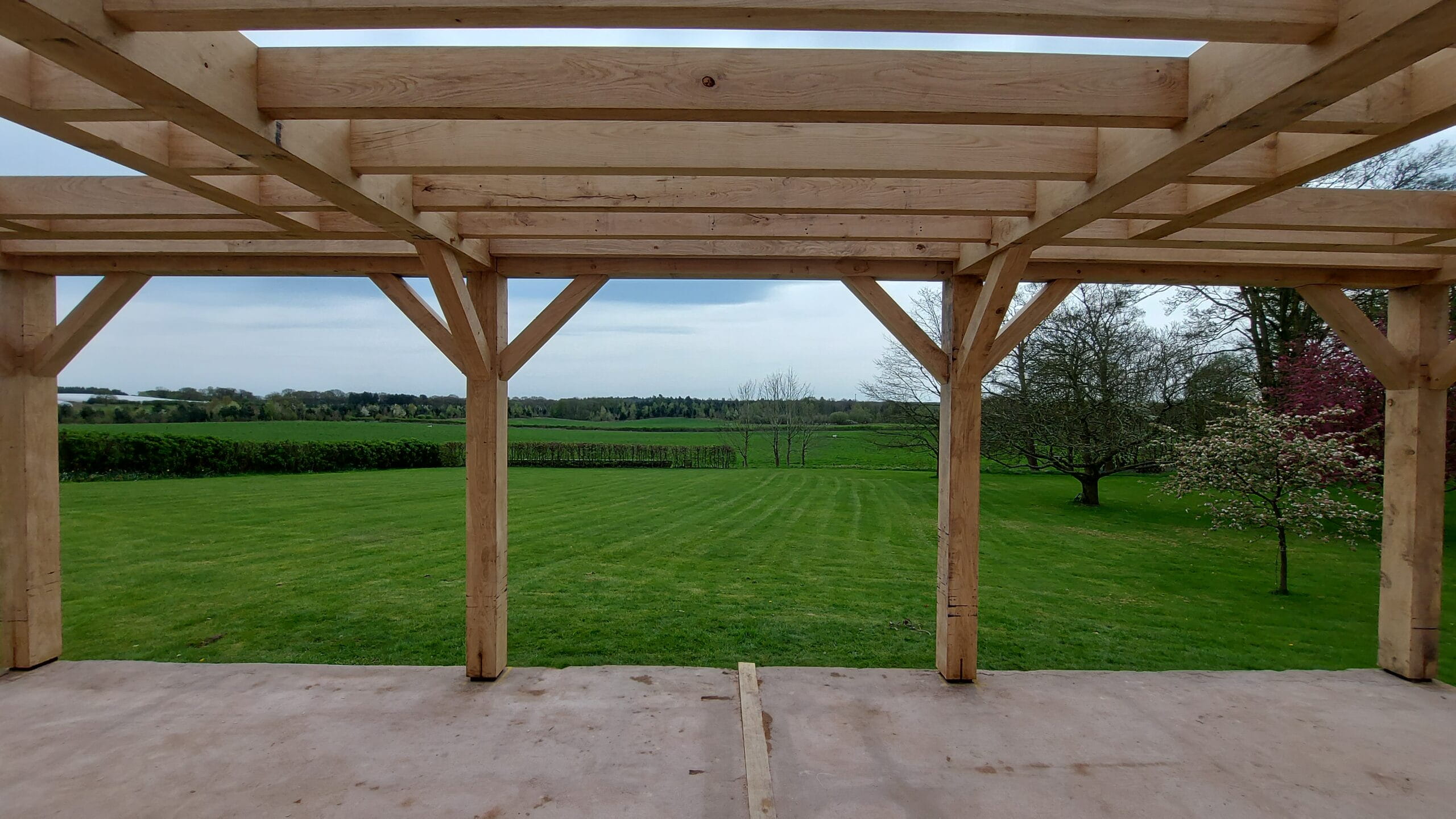 A view from inside a newly constructed Douglas Fir timber frame building looking out onto a large green lawn and countryside.