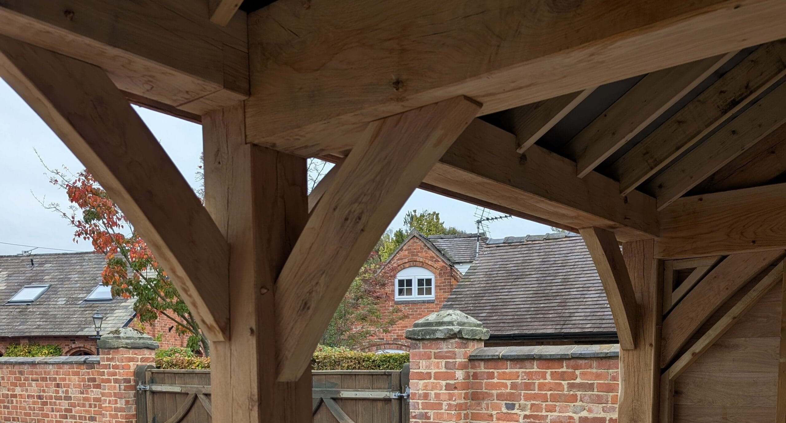 Close-up of a traditional British green oak timber frame showing the interlocking beams and curved braces of an outdoor structure.